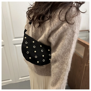 Detail of black suede crescent bag with gold rivets and ring accents on a model