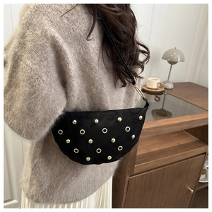 Detail of a crescent black suede shoulder bag with gold rivets and metallic rings