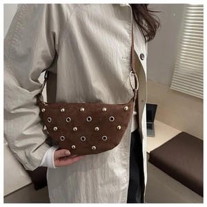 Detail of suede half-moon bag with golden rivets and metallic eyelets on shoulder strap