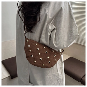Detail of brown suede crescent bag with metallic eyelets and studs in a lifestyle setting