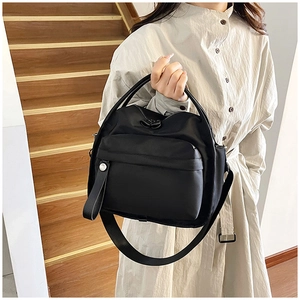 Detail of a black nylon handbag with silver zippers shown on a model in casual attire