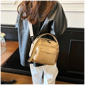 Close-up of khaki nylon crossbody bag showing the front zipper pocket and canvas strap