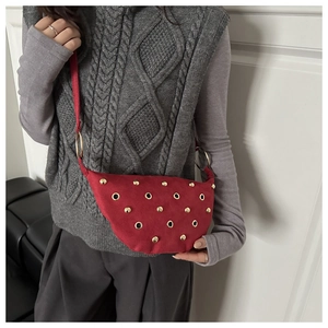 Detail of red suede crescent bag featuring golden rivets and metal ring embellishments