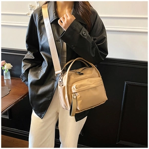Close-up of beige nylon crossbody bag with wide strap and multi-pocket design on model