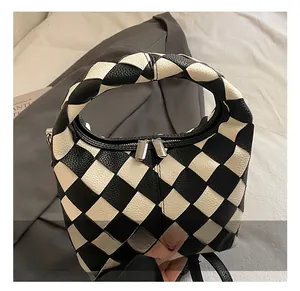 Detail of black and white checkered woven handbag with silver metal zippers and hardware