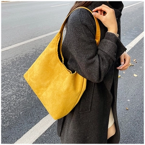Detail of yellow suede tote bag shoulder strap and seam texture against a dark grey coat