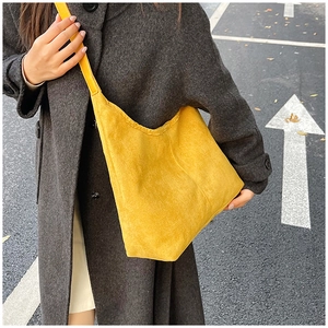 Outdoor street style shot of a yellow corduroy hobo tote bag worn with a grey wool coat