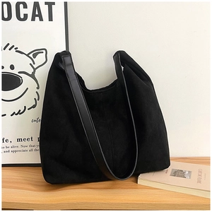 Detail of a black suede tote bag with leather strap on a minimalist wooden table