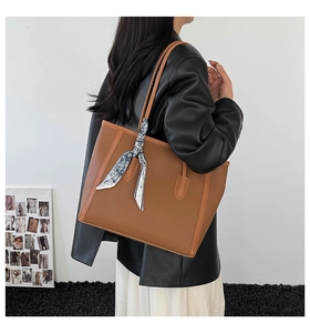 Détail de sac cabas en cuir grainé marron avec foulard en soie décoratif sur la poignée