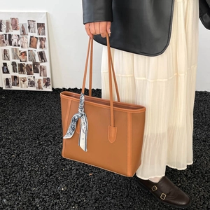 Detail of tan leather tote bag with a silk scarf handle wrap against a minimalist wall