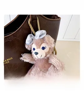 Close-up of a plush bear charm with a striped bow on a brown pebbled leather tote bag