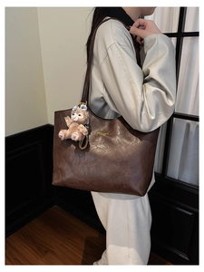 Detail of dark brown vintage leather tote with gold logo and plush bear charm accent