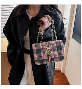 Detail of red and black plaid crossbody bag with golden S-lock and chain strap