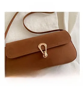 Close-up of brown suede shoulder bag with elegant golden horseshoe metallic twist lock
