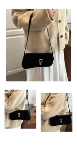 Detail of black suede baguette bag with golden horseshoe buckle and slim shoulder strap