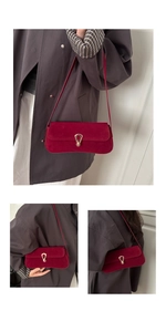Detail of burgundy suede baguette bag with gold horseshoe buckle on grey coat