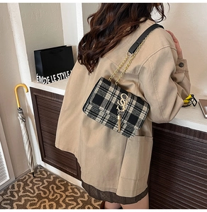 Close-up of black and white plaid tweed handbag with gold letter charm and metal chain