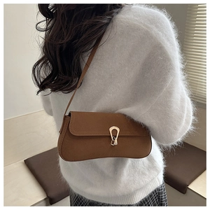 Close-up of brown suede baguette bag with golden horseshoe buckle worn by a model