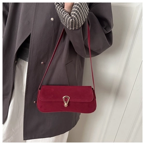 Detail of burgundy suede shoulder bag with gold horseshoe buckle on grey coat
