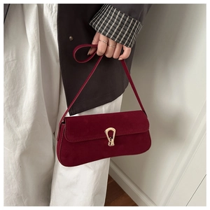Close-up of burgundy suede baguette bag with golden horseshoe buckle held by model