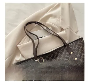 Detail of brown leather tote with M-pattern print and a white cloud plush charm