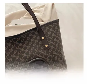 Detail of dark brown tote bag with M-pattern monogram, logo, and plush bear charm