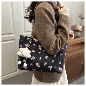 Close-up of black floral tote bag with pink bows and a plush cloud charm accessory