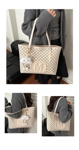 Detail of cream tote bag with repetitive M letter print and plush cloud charm accessory