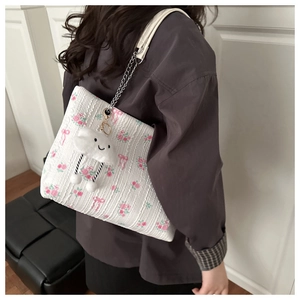 Detail of floral tote bag with silver chain strap and cloud plush charm on shoulder