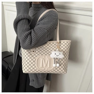 Fashionable beige tote bag with M-letter print and plush cloud charm on a model