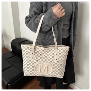 Détail d'un sac cabas beige avec imprimé lettres M et logo porté par un mannequin