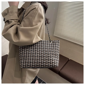 Detail of tweed woven shoulder bag with metal chain strap on model wearing trench coat