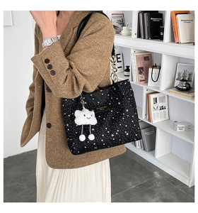 Star pattern black tote bag with white cloud charm and leather straps in bookshelf setting