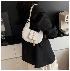 Detail of a beige crescent moon bag with gold S logo and tassels worn by a model