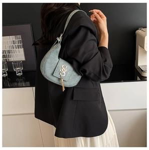 Detail view of sage green saddle bag with metallic SS buckle and tassel decoration