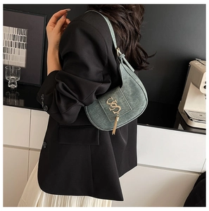 Detail of green textured half-moon bag with gold logo and tassel on model's shoulder