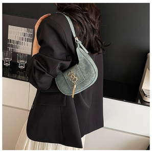 Detail of dark green crescent shoulder bag with gold metal logo and fringe on a model