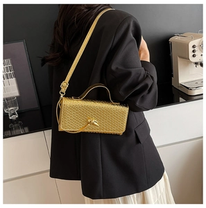 Detail of gold woven handbag with knotted accent worn by model in elegant setting