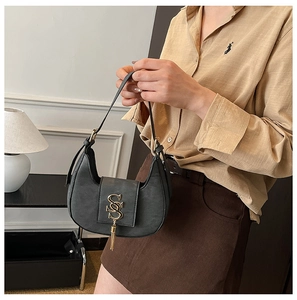Detail of black matte croissant bag featuring gold logo and metallic tassel charm