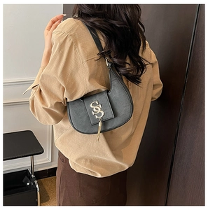 Detail of black crescent shoulder bag with gold metal logo and tassel on a model