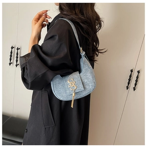 Detail of light blue wool crescent bag with gold SS logo and tassel on black coat