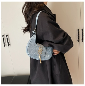 Close-up of light blue dumpling bag featuring gold S logo and elegant metal tassel