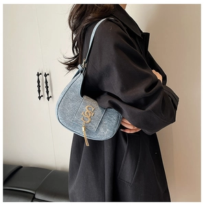 Detail of blue denim crescent bag with golden S-logo hardware and elegant tassel detail
