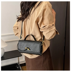 Detail of black woven texture handbag with golden twist lock on beige shirt outfit