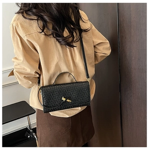 Detail of black woven leather texture and gold knot metal clasp on a stylish square bag