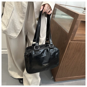 Détail d'un sac cabas en cuir verni noir avec longues anses et plaque de marque en métal