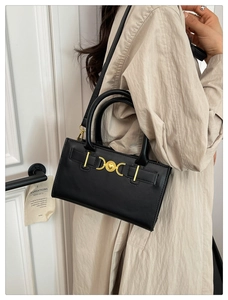 Dettaglio borsa a tracolla in pelle nera con fibbia a cuore dorata e trench beige