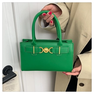 Dettaglio borsa a mano verde con chiusura a cuore dorata tenuta da modella in cappotto beige