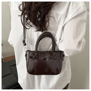 Detail of dark brown glossy patent leather crossbody bag on white shirt background