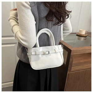 Close-up of white crossbody box bag featuring front buckle strap and top double handles
